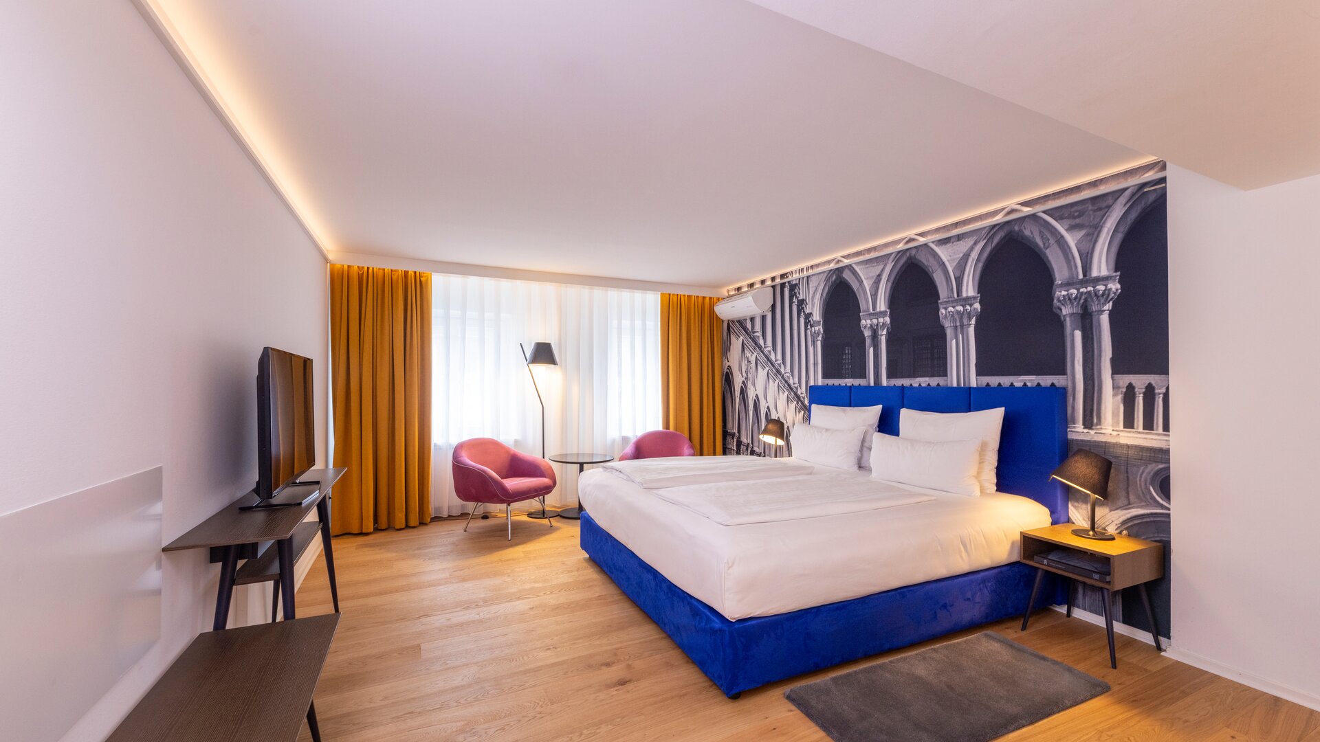 Junior Suite Overview with Blue, Pink, and Yellow Accents Decor, and with Accent Wall of Black & White Mural Wall Paper of Decorative Arches