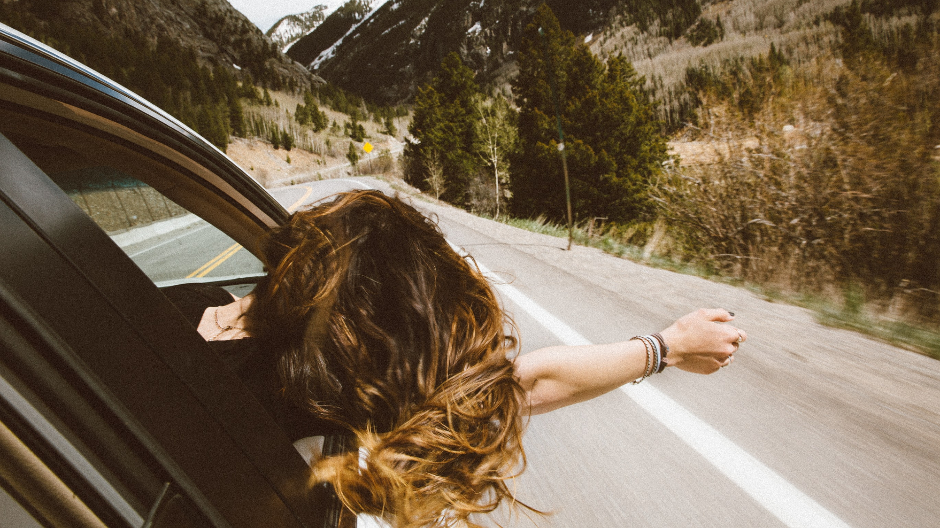 woman sticking hand out moving car window to feel the air between her fingers