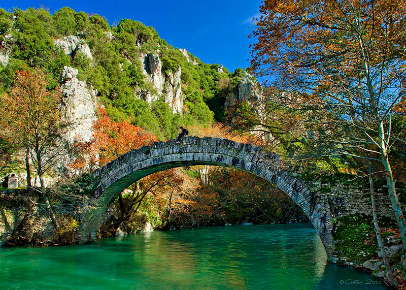 A traditional stone bridge spans the Voidomatis River.
