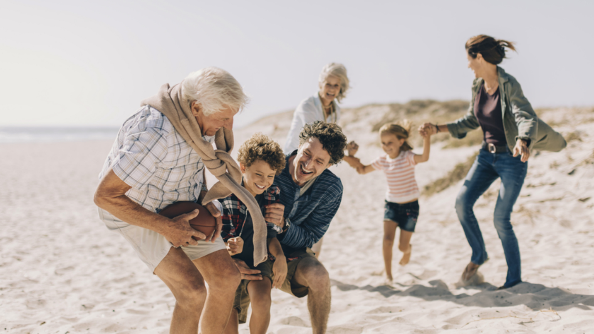 multigenerational family playing on beach at sunset