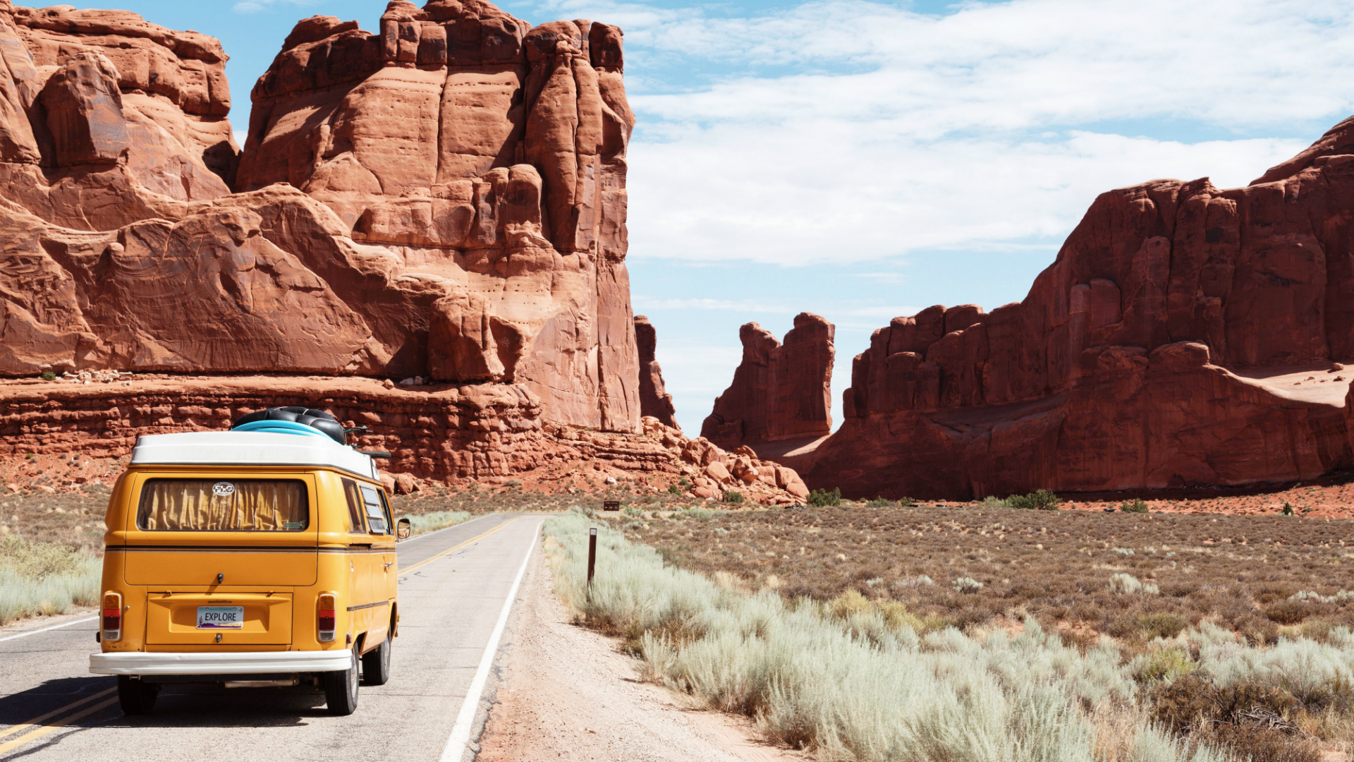 yellow vw wagon driving through desert landscape in american southwest road trip