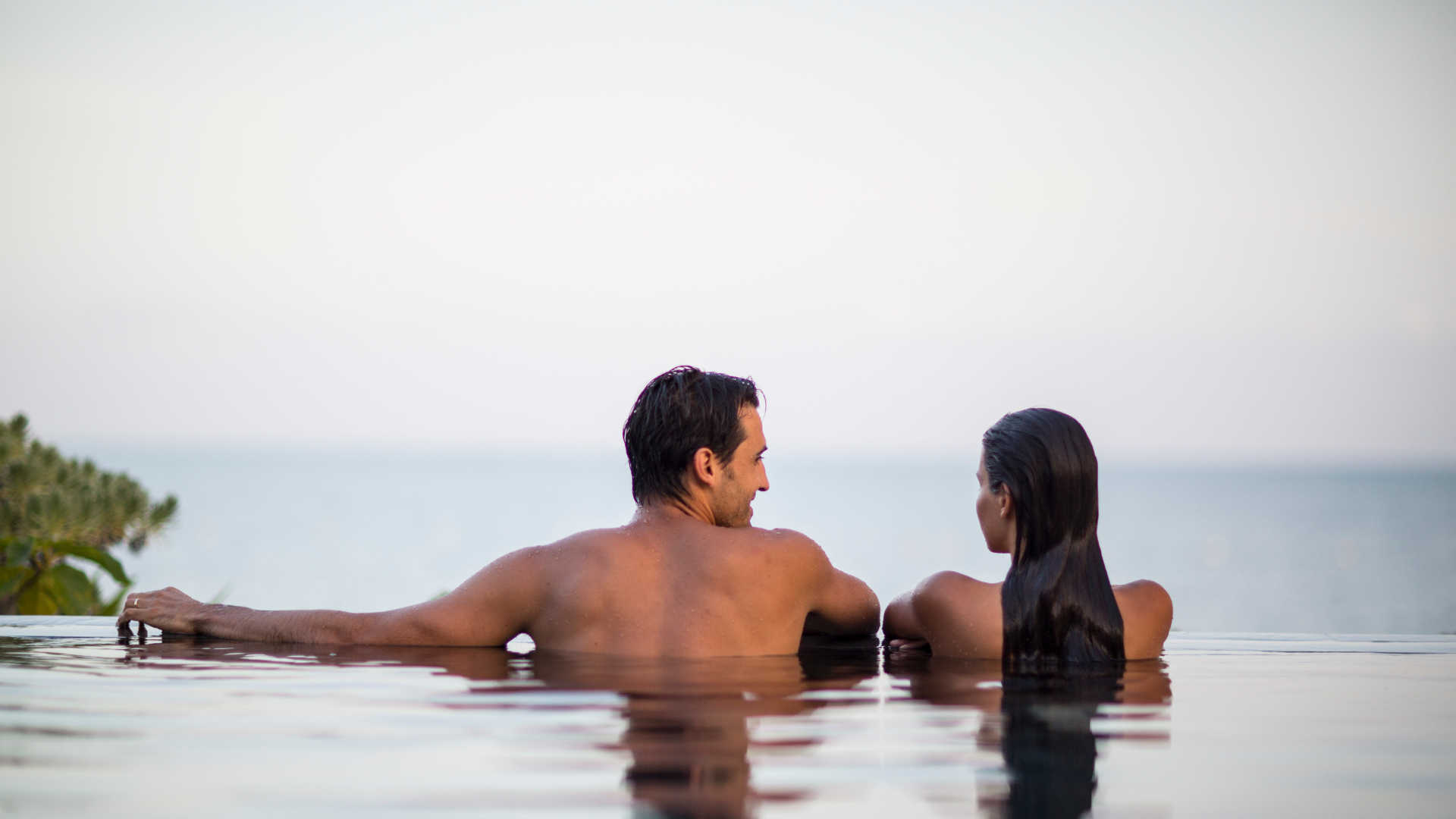 couple in infinity pool overlooking ocean in distance
