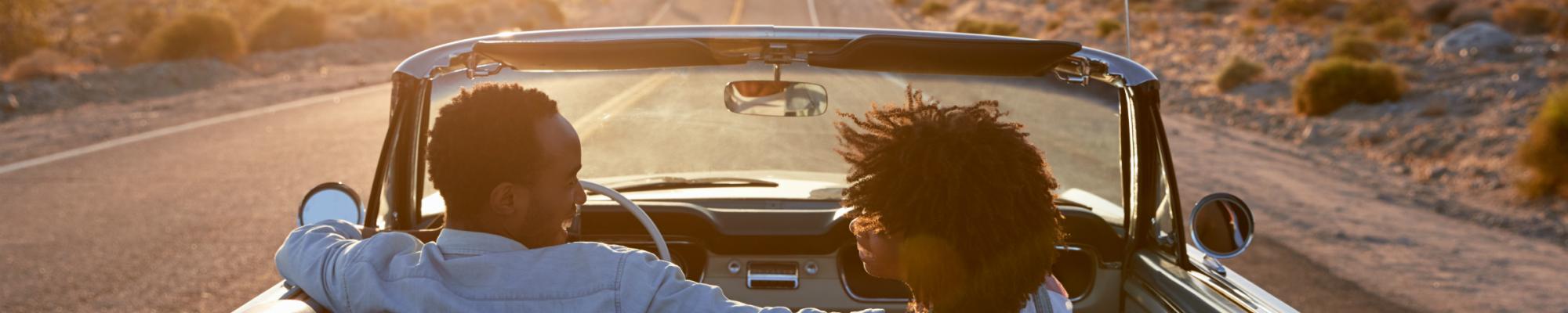 black couple in covertible driving down desert highway into sunset road trip 