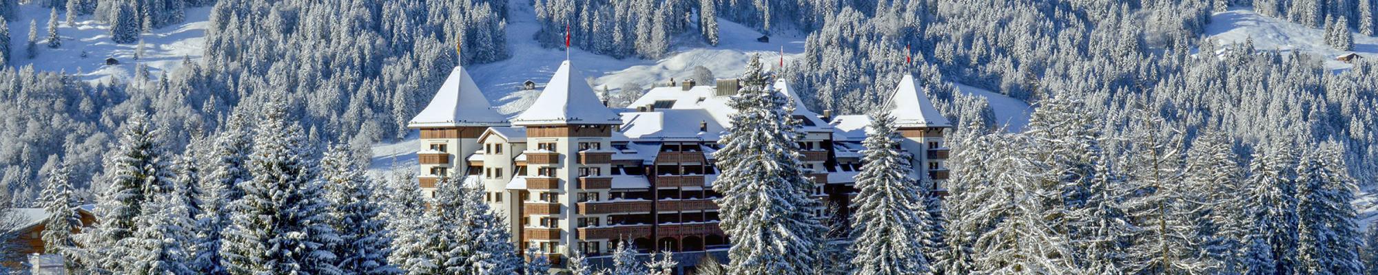 The Alpain Gstaad hotel from a distance with rooftops covered with snow and fir trees in the foreground
