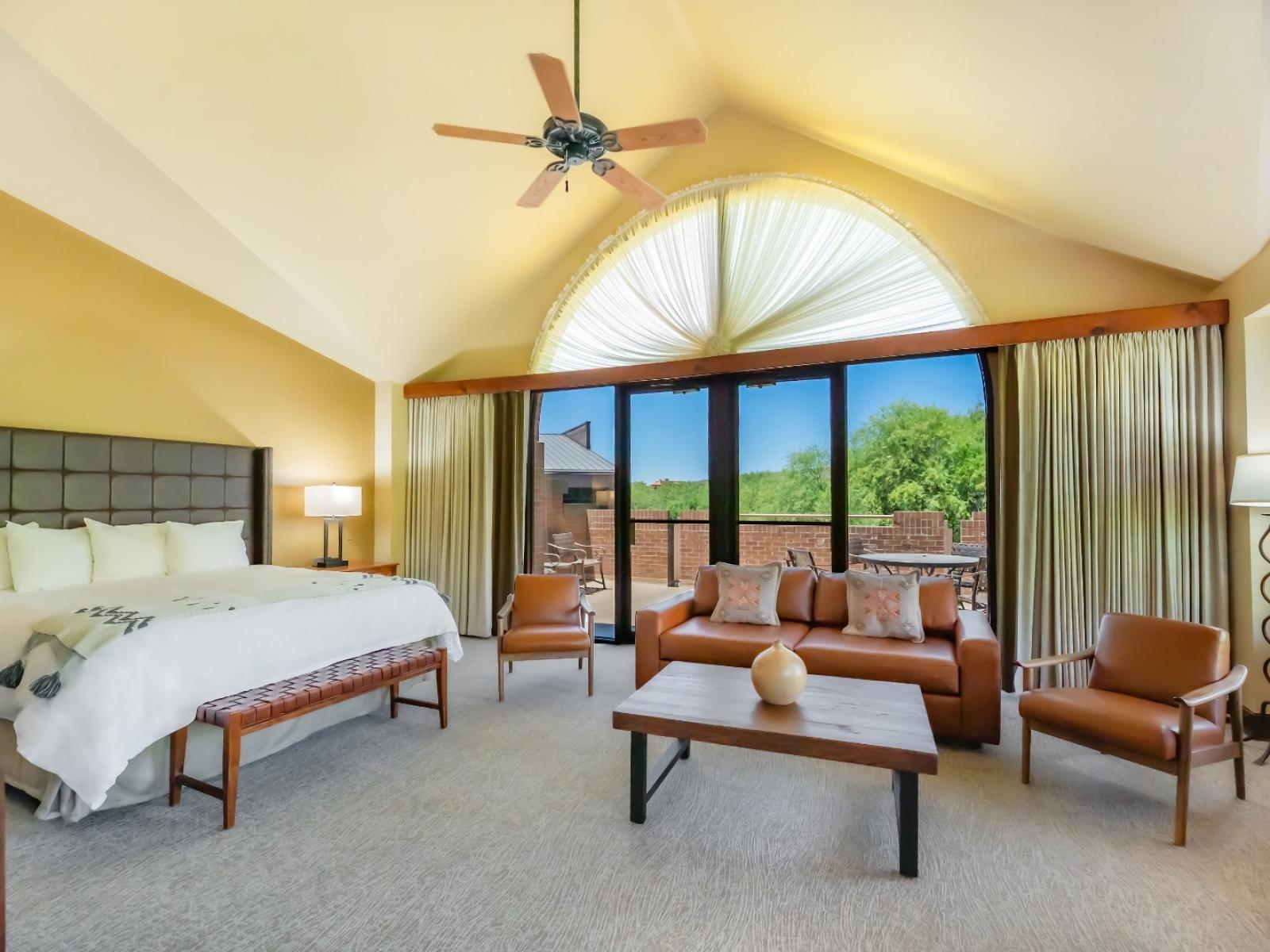 A king bed with couch and seating area, and balcony window behind it. 