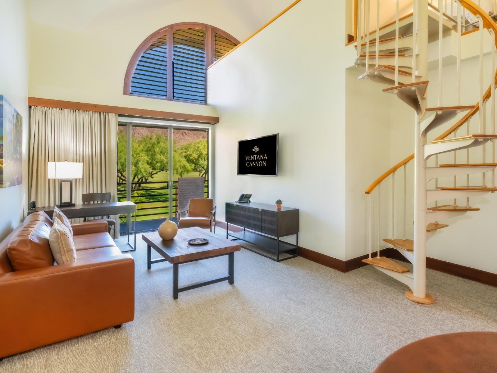 The living room from the Deluxe Suite, showing the television, seating area, and spiral staircase to the loft. 