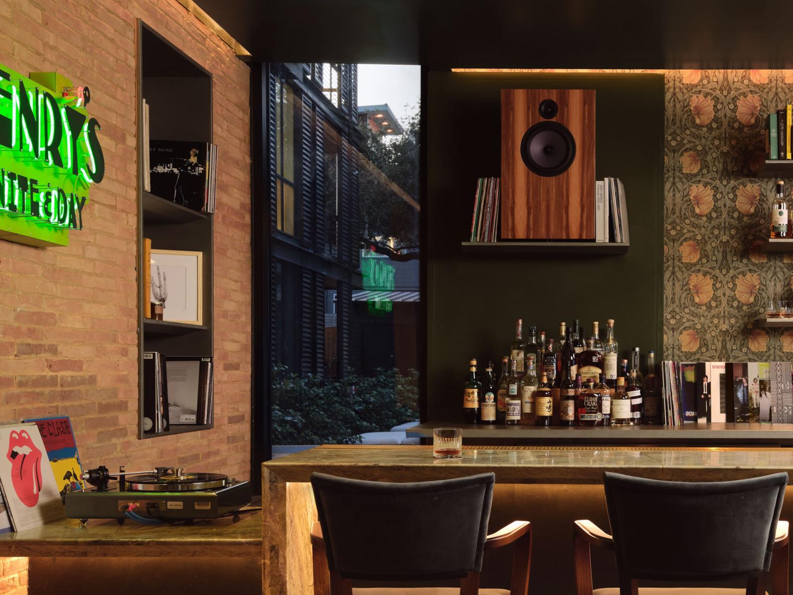 The Inn at Green Pastures, Henry’s stylish bar featuring a sleek marble counter, curated spirits, warm brick accents, and a vibrant neon sign for an inviting, modern vibe.
