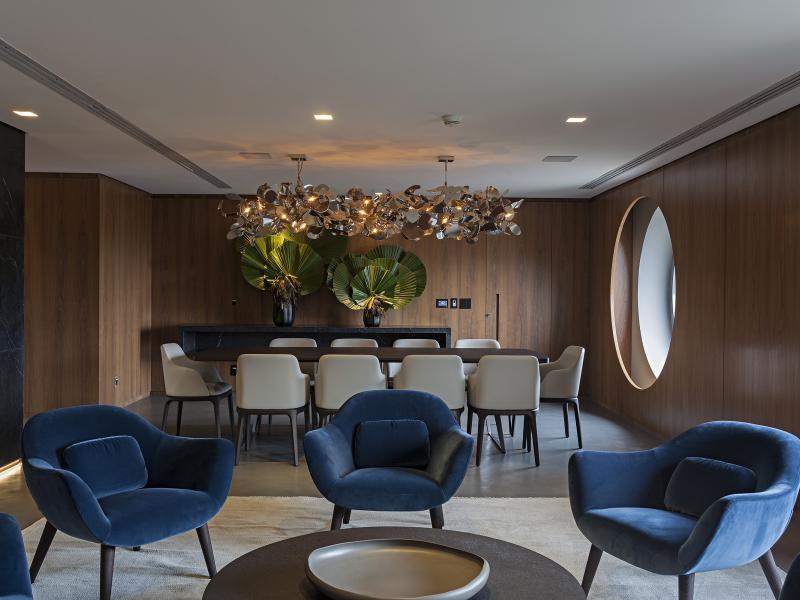 Oasis suite modern dining and lounge area featuring plush navy chairs and a statement chandelier, complemented by rich wood paneling and vibrant green foliage accents.