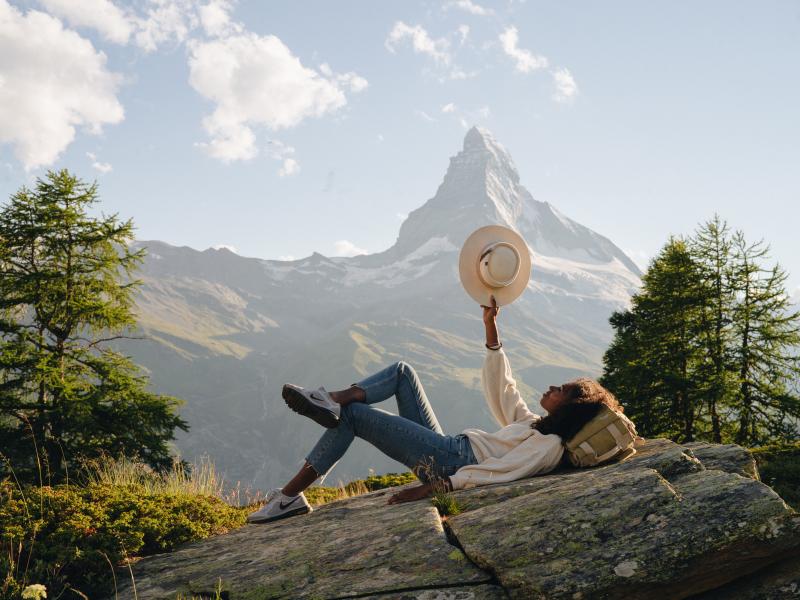 Woman laying on rocks during hike, holding hat above her.