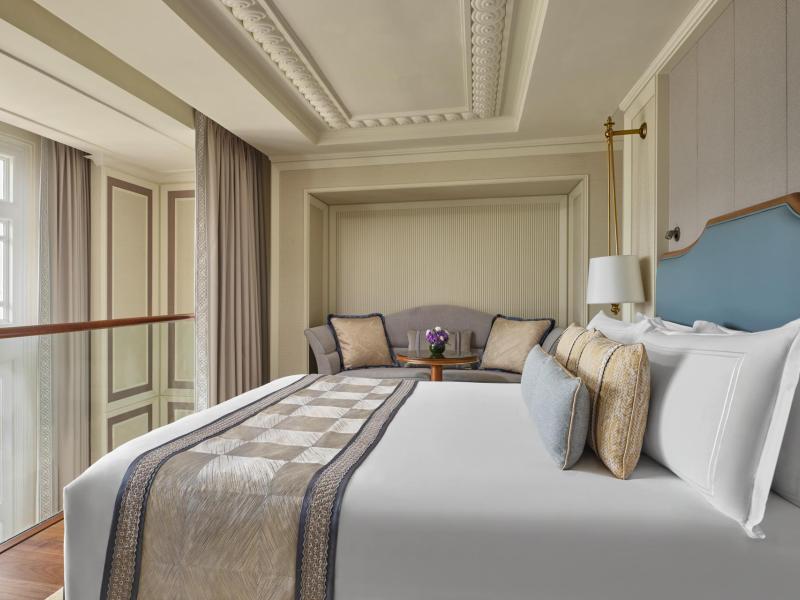 This serene bedroom in a Loft Suite pairs a tailored bed and detailed ceiling moldings with soothing blue, beige, and ivory accents for a calm, upscale ambiance.