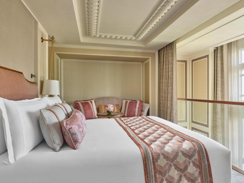 The Fullerton Hotel Singapore elegant Loft Suite bedroom features a plush bed with layered bedding, coffered ceilings, and soft blush and cream accents for a refined, restful feel.