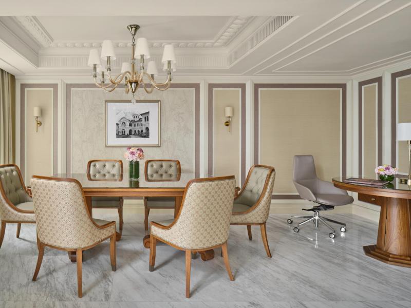 A sophisticated dining space of a Loft Suite highlights a statement chandelier, upholstered chairs, and paneled walls in neutral cream tones with subtle blush accents.