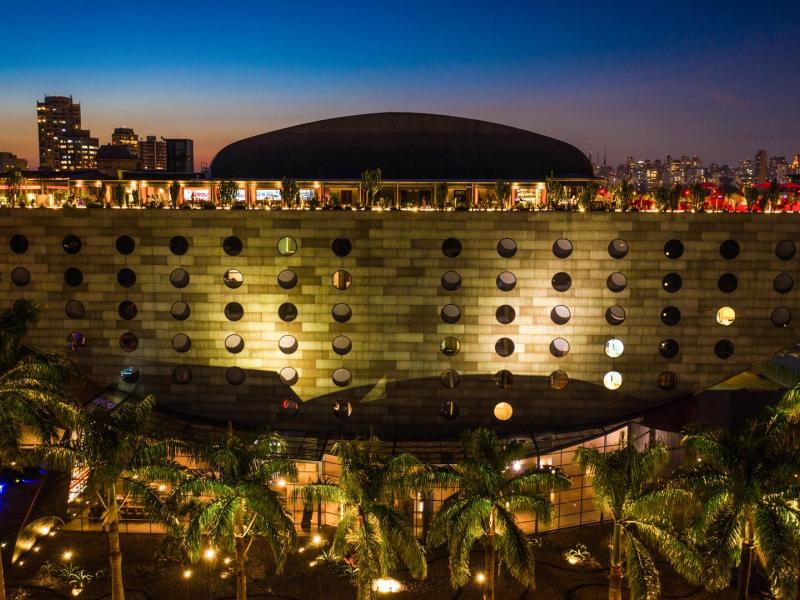 Hotel Unique exterior showcasing a striking circular-window façade illuminated in warm golden tones with lush green palm accents against a deep blue twilight skyline.