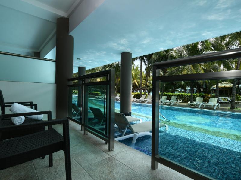 Oceanfront One Bedroom Suite private terrace with chairs overlooking serene pool lined with palm trees.