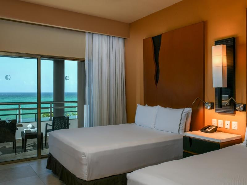 Oceanfront One Bedroom Swim Up Suite with two double beds opens onto a balcony overlooking a turquoise ocean view.