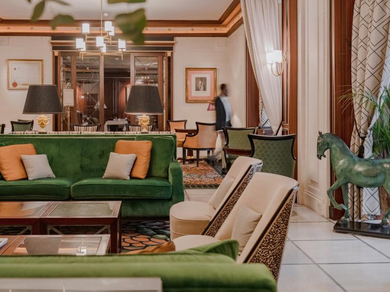 Stylish lobby featuring plush green sofas, warm wood accents, and pops of orange and cream for a vibrant yet elegant setting.