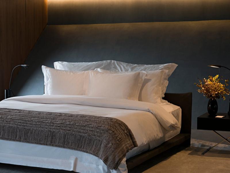 Oasis suite tranquil bedroom with a round picture window and sleek black bedside lamps, accented by deep charcoal walls and warm wood tones.