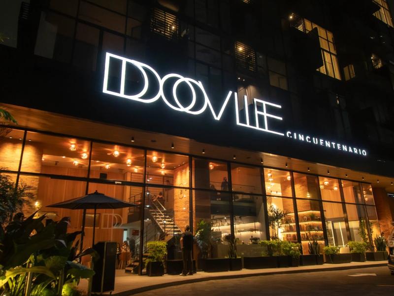 Dovle Branded Residences striking nighttime facade with bold illuminated signage and floor-to-ceiling glass showcasing a warm, inviting interior.