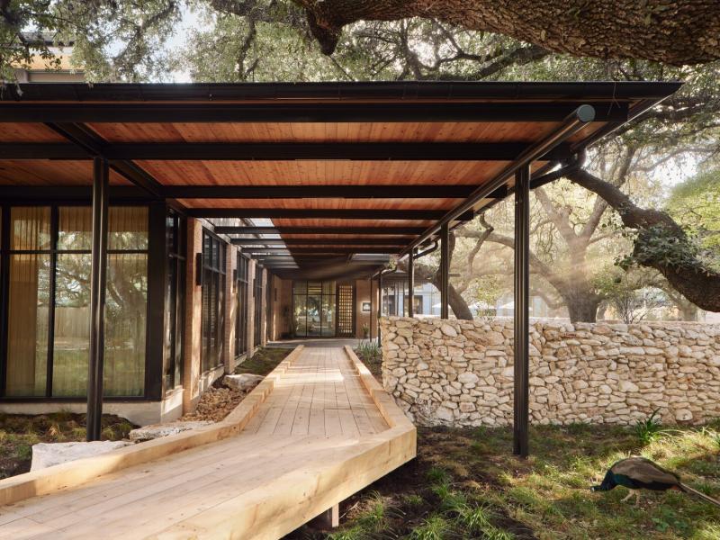 The Inn at Green Pastures stunning exterior entryway featuring a sleek wooden walkway, modern steel-and-glass architecture, and natural stone accents surrounded by lush forest for an inviting, contemporary feel.