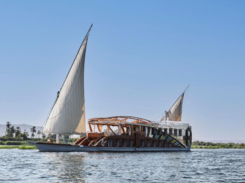 Sail in style aboard Mazaj Seba traditional wooden vessel with elegant twin sails, gliding across serene waters under a clear blue sky.