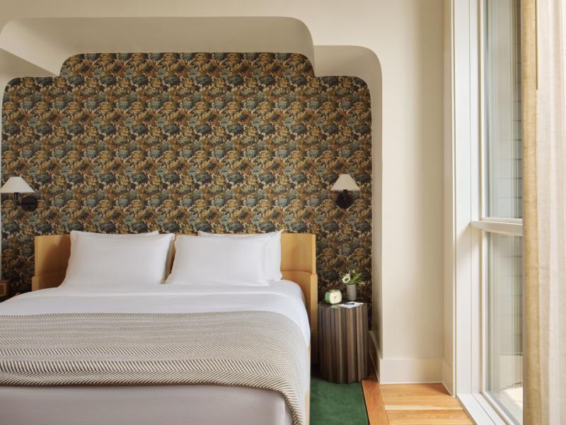 Stylish king guest room featuring a plush bed with crisp white linens, a bold patterned accent wall, warm wood flooring, and floor-to-ceiling windows for abundant natural light.