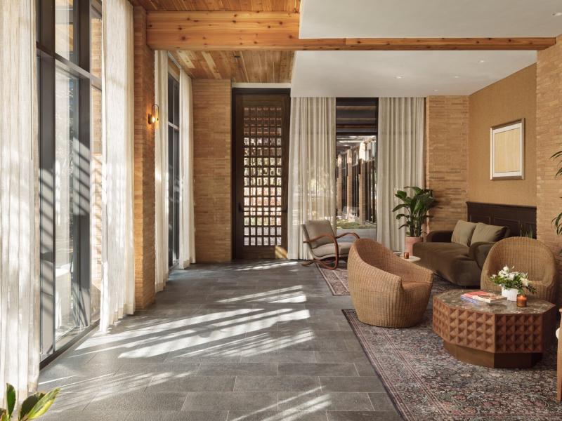 Inviting lobby featuring warm brick walls, floor-to-ceiling windows with sheer drapes, stylish lounge seating, and elegant décor accented by lush plants.