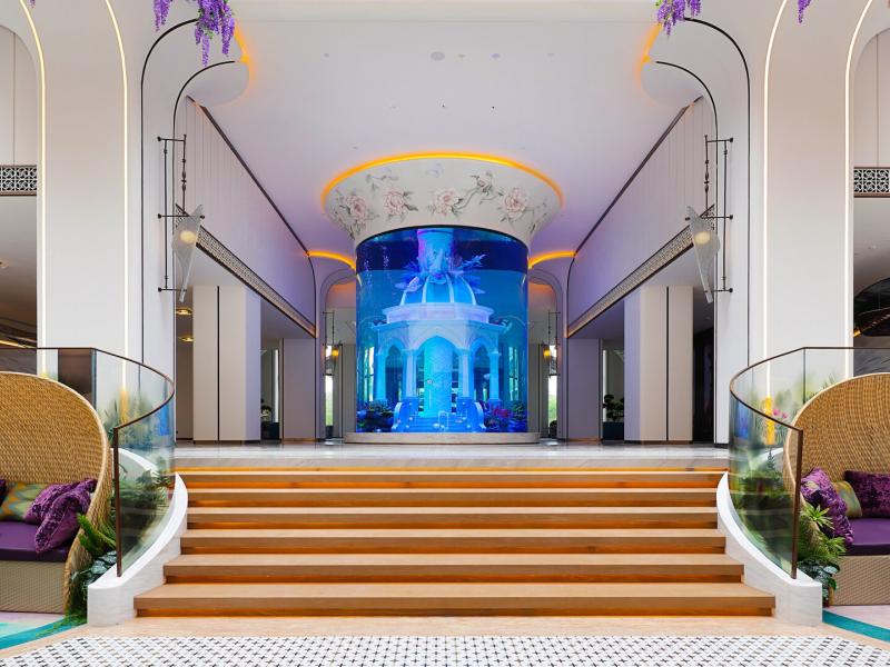 Elegant lobby featuring a grand cylindrical aquarium centerpiece, surrounded by modern seating areas and vibrant decorative accents.
