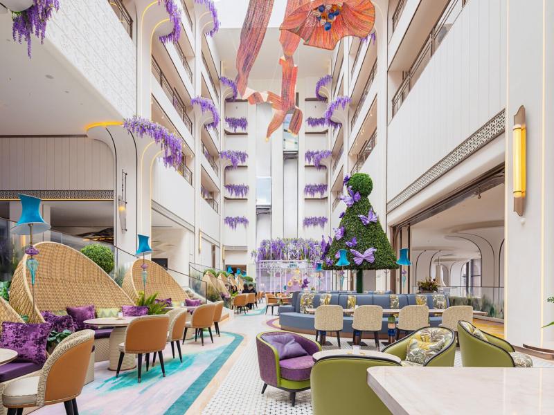 Vibrant lobby lounge adorned with cascading purple floral decor, colorful seating, and whimsical artistic installations creating a lively and elegant atmosphere.