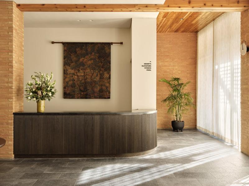 Elegant lobby reception area featuring a sleek curved desk, warm wood accents, floor-to-ceiling sheer drapes, and lush greenery for a sophisticated first impression.