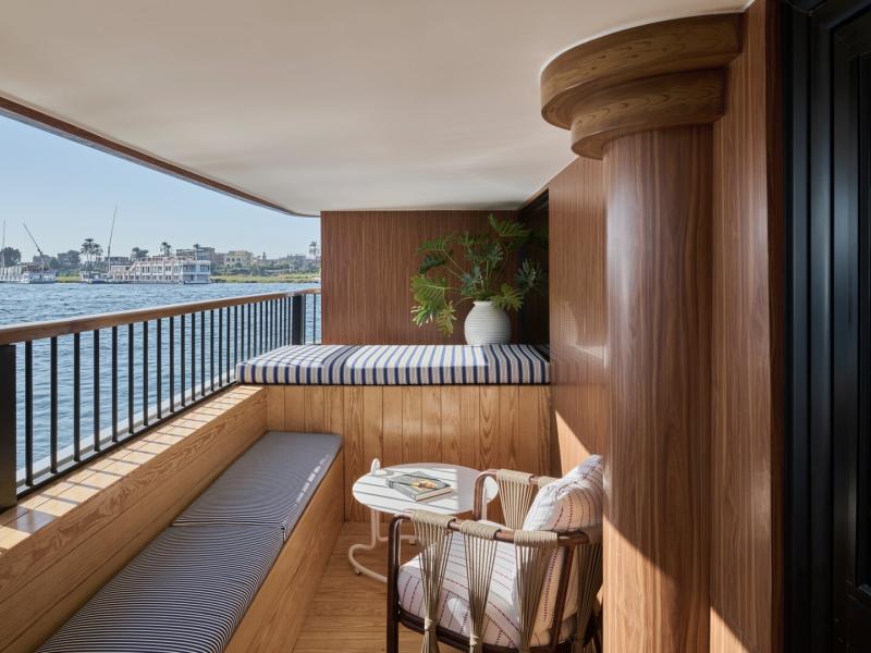 Suite intimate, wood‑paneled balcony lounge with a striped daybed, built‑in seating, and riverside views.