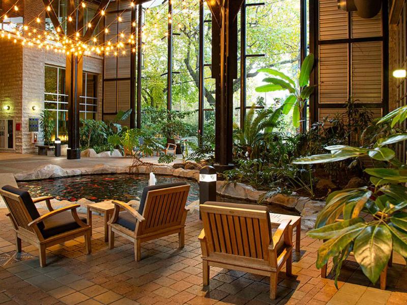 Elegant atrium with cozy wooden seating, warm ambient lighting, and a serene coy pond framed by floor-to-ceiling windows.