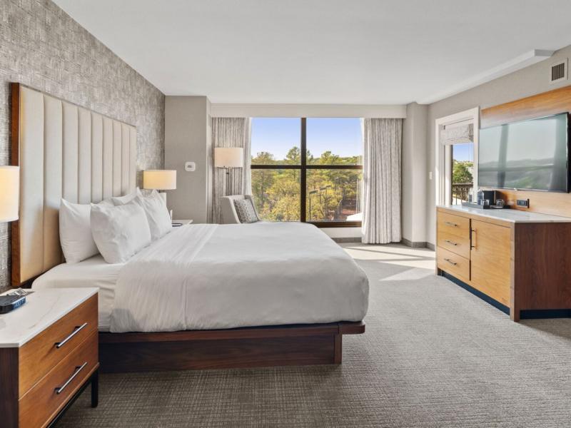 An elegantly appointed bedroom of a Junior Suite showcases a plush king bed with crisp linens, bespoke modern furnishings, and floor-to-ceiling windows framing serene panoramic views for an indulgent escape.