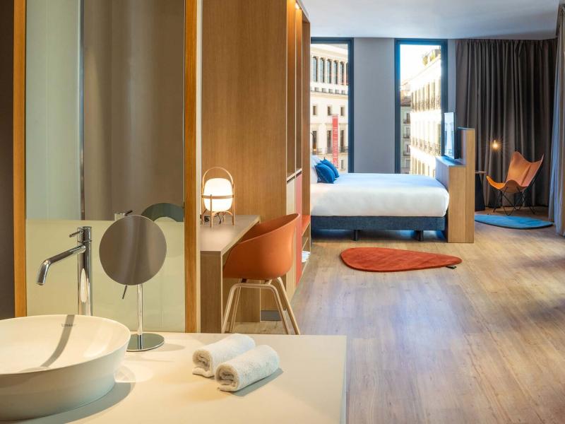 Spacious, light-filled Superior Garden View Guestroom with elegant wood accents, a modern open bathroom, and stunning city views of Madrid.