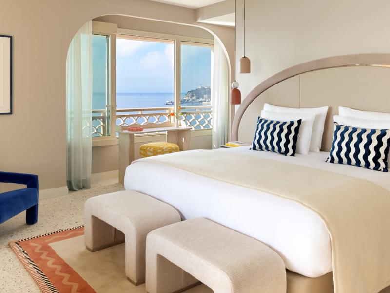 The Prestige Duplex Suite - Sea View serene, modern bedroom with a plush bed and bold accent pillows opens onto a balcony with breathtaking views of the sea and Monaco’s coastline.
