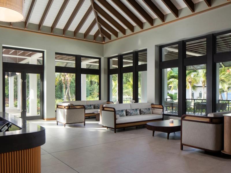 The airy lobby with soaring wood‑beam ceilings and expansive black‑trim windows, accented by soft beige seating and warm natural light.