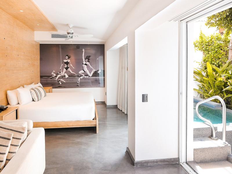 Poolside Villa stylish bedroom with a king bed and modern wall art, featuring warm beige tones and crisp white accents, opening to a private pool framed by lush greenery.