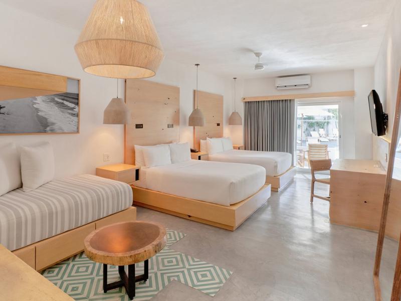 Spacious Poolside Double Suite with three beds, natural wood furnishings, and woven pendant lights, accented by soft gray flooring and mint-green geometric details.