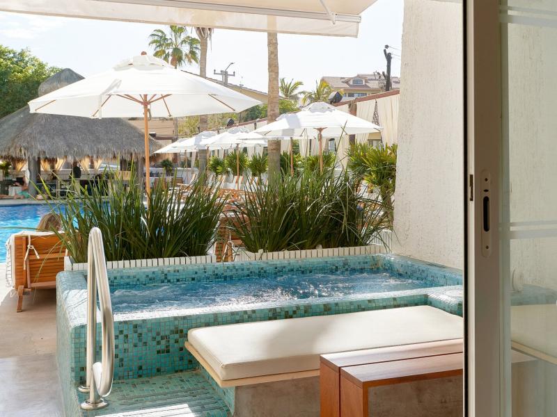 Serene private terrace and Jacuzzi of a Poolside Suite with turquoise mosaic tiles and cushioned seating, complemented by fresh greenery and bright white umbrellas for a relaxing escape.