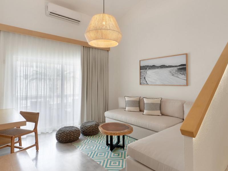 A cozy lounge area of a loft featuring a neutral sofa and woven pendant lamp, complemented by earthy brown poufs and a mint-green patterned rug.