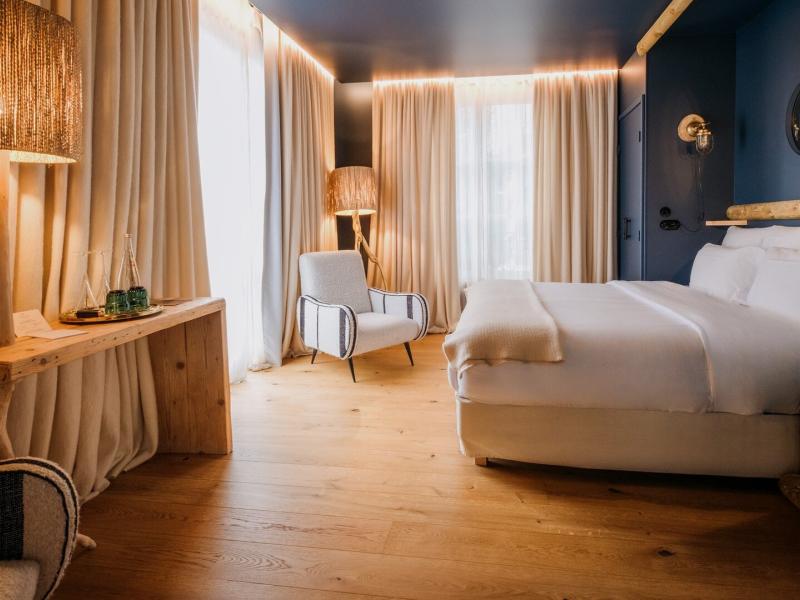 A Chalet bedroom featuring sleek navy walls and warm wood flooring, this stylish room is accented with soft beige drapes and natural wood details.