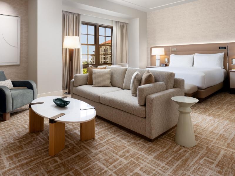 A spacious Executive King Suite bedroom featuring a plush beige sofa and king bed, accented by warm taupe walls and crisp white linens.