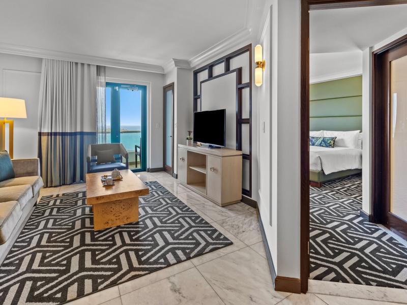 Biltmore spacious suite with a cozy seating area, sleek black-and-white patterned rugs, marble flooring, and a private balcony offering panoramic ocean views.
