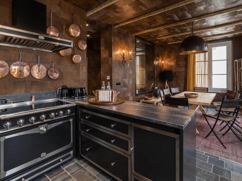 A Chalet kitchen designed with dark cabinetry and copper accents, featuring a stone floor and warm golden lighting.