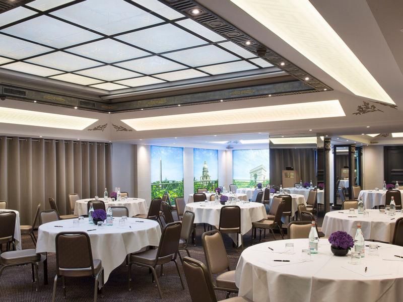 Friedland Room bright meeting space featuring round tables with crisp white linens, accented by purple floral centerpieces and soft gray tones.