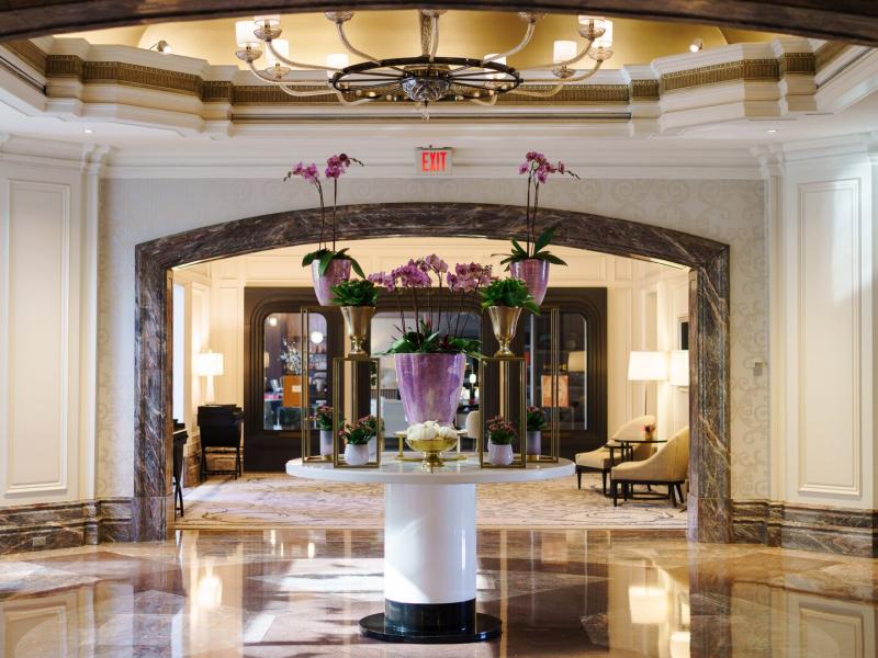 Boston Harbor Hotel grand lobby featuring polished marble floors and ornate archways, highlighted by soft ivory walls and vibrant purple floral accents.