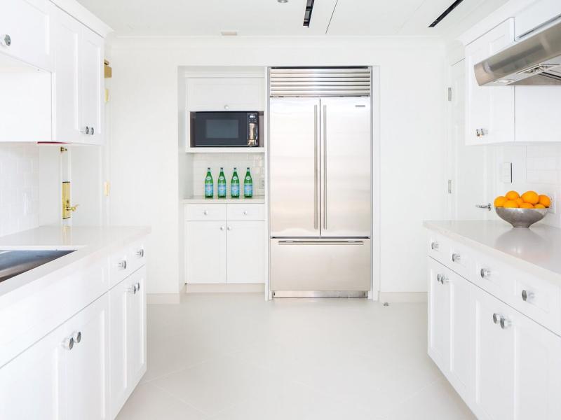 John Adams Presidential Suite sleek white kitchen featuring stainless steel appliances and crisp cabinetry accented by vibrant green bottles and a pop of orange from fresh fruit.