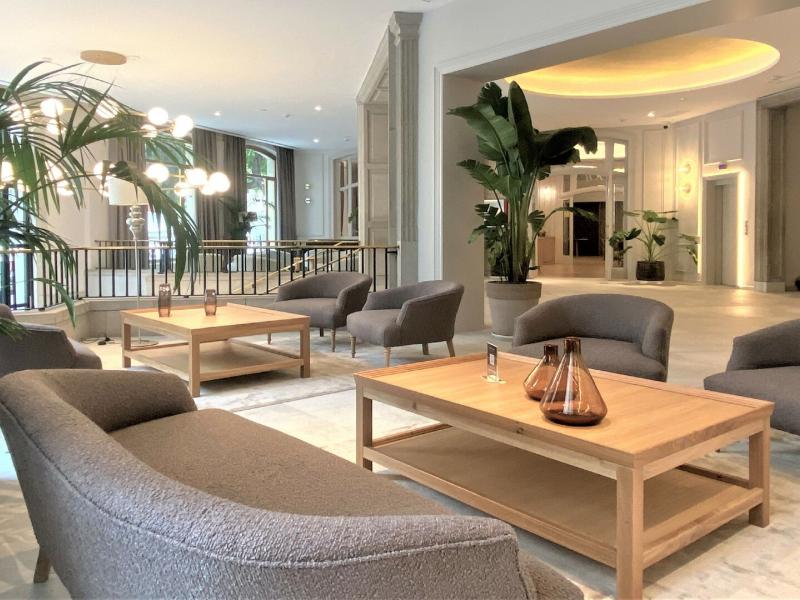 Lamaro Hotel modern lobby with sleek gray seating and natural wood tables, accented by vibrant green plants and soft golden lighting for a welcoming ambiance.
