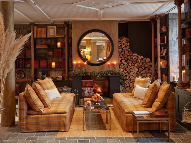 Featuring cozy plaid sofas in warm amber hues, Grand Hôtel Soleil d’Or lobby is accented with rustic wood shelves, glowing candles, and earthy beige details.