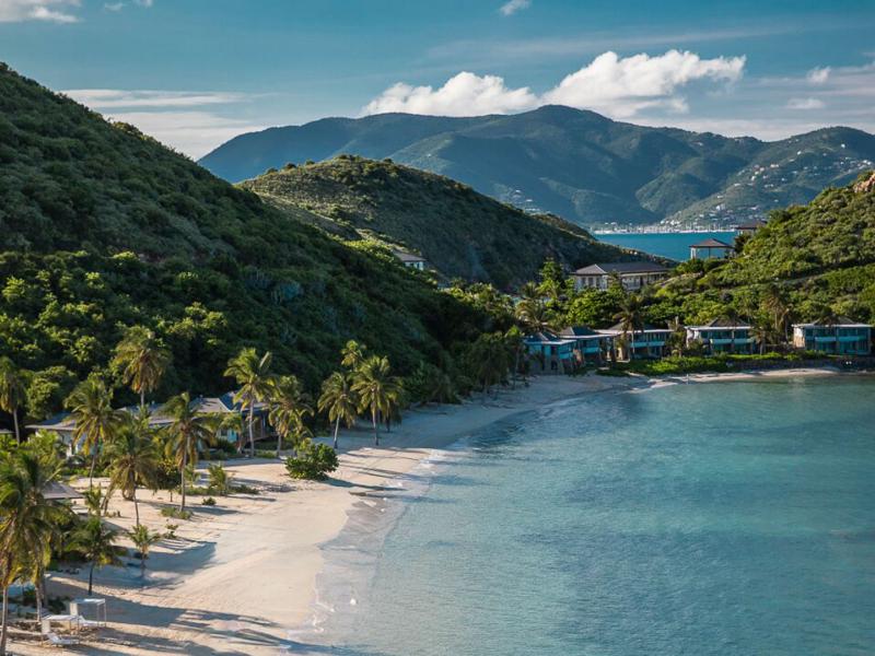 Pristine Deadman's Beach lined with emerald palms and turquoise waters, accented by ivory sand and vibrant blue villas nestled in the hills.