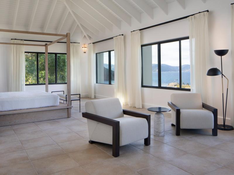 Hawk's Nest airy primary bedroom with vaulted white ceilings and panoramic windows, accented by soft beige flooring and sleek black frames.